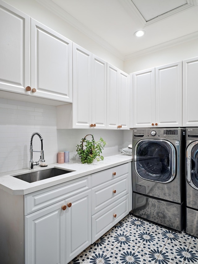 clothes washing area with cabinets, crown molding, sink, and washer and clothes dryer