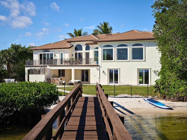 back of property featuring a lawn, a balcony, and a water view