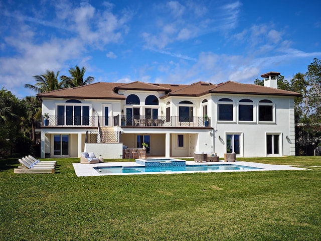 rear view of property featuring a swimming pool with hot tub, a lawn, a balcony, and a patio area