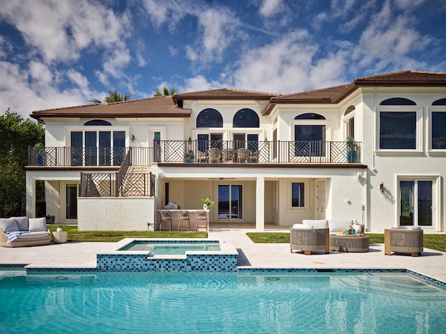 back of house with a balcony, a swimming pool with hot tub, an outdoor hangout area, and a patio