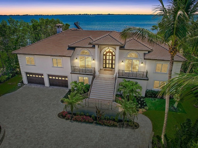 view of front facade with a garage, a balcony, a water view, and french doors