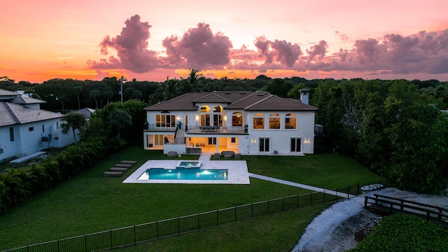 back of house at dusk featuring a lawn, a fenced backyard, a balcony, a fenced in pool, and stairs