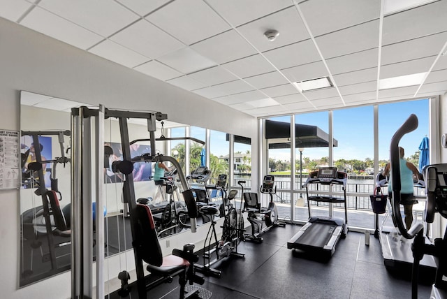 workout area with expansive windows, a paneled ceiling, and a water view