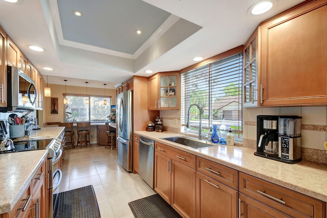 kitchen with glass insert cabinets, appliances with stainless steel finishes, brown cabinets, a tray ceiling, and a sink