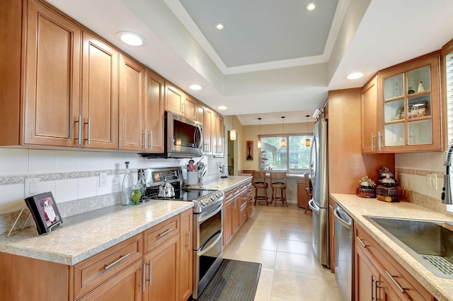 kitchen featuring stainless steel appliances, brown cabinetry, a raised ceiling, and decorative backsplash