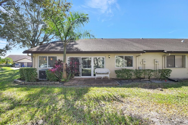 rear view of house with a yard, a shingled roof, cooling unit, and stucco siding