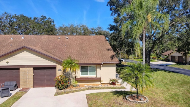 view of front of house featuring roof with shingles, brick siding, an attached garage, a front yard, and driveway