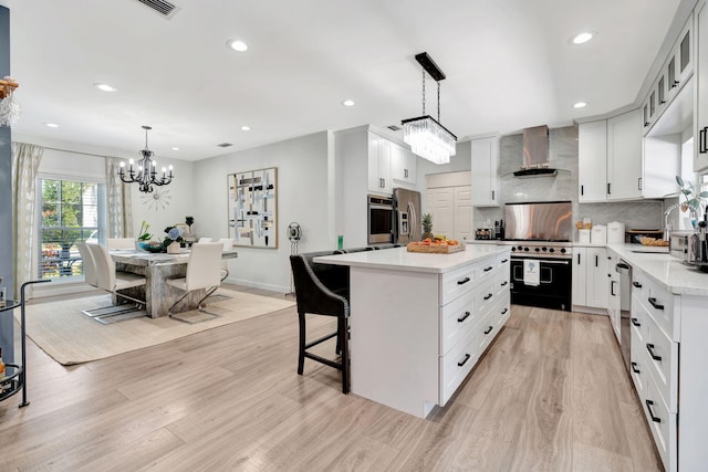 kitchen featuring decorative light fixtures, white cabinets, a center island, stainless steel appliances, and wall chimney range hood