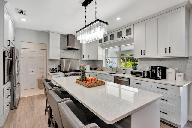 kitchen featuring wall chimney exhaust hood, a center island, sink, and white cabinets