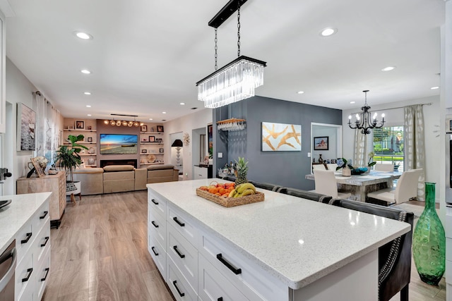 kitchen featuring white cabinetry, hanging light fixtures, light stone counters, a kitchen island, and light wood-type flooring