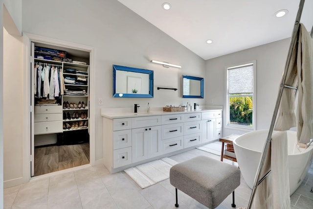 bathroom with lofted ceiling, vanity, a bathtub, and tile patterned flooring