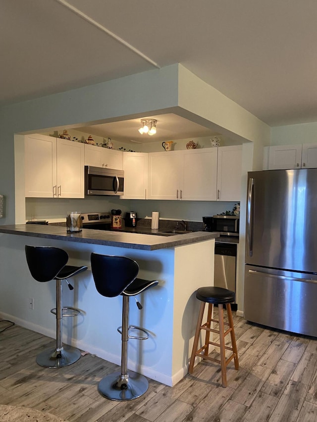 kitchen featuring white cabinetry, stainless steel appliances, a kitchen breakfast bar, and light wood-type flooring