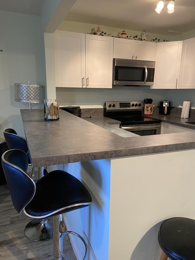 kitchen featuring white cabinetry, stainless steel appliances, kitchen peninsula, and a kitchen bar