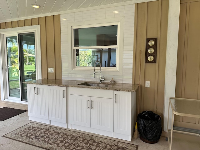 bar featuring wood walls, dark stone counters, sink, and white cabinets