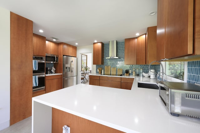 kitchen with appliances with stainless steel finishes, tasteful backsplash, sink, kitchen peninsula, and wall chimney range hood