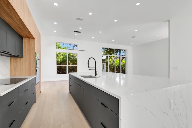 kitchen featuring sink, gray cabinets, multiple ovens, black electric stovetop, and decorative light fixtures