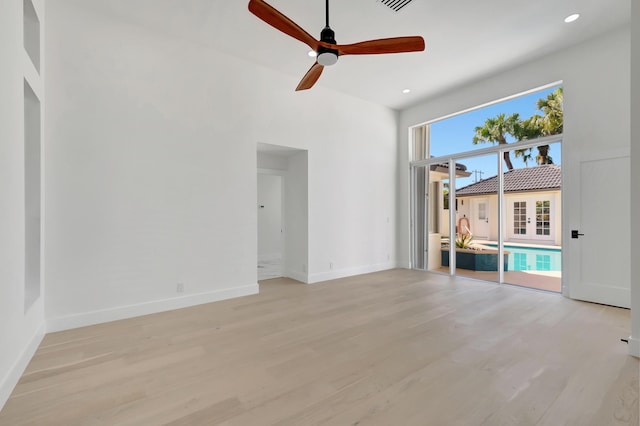 unfurnished living room with a towering ceiling, ceiling fan, and light wood-type flooring