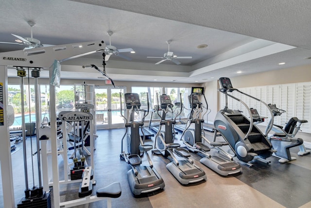 exercise room featuring ceiling fan, a tray ceiling, and a textured ceiling