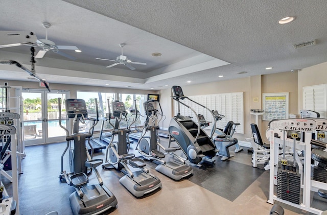 exercise room featuring a raised ceiling, ceiling fan, french doors, and a textured ceiling