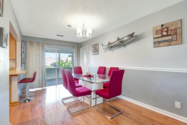 dining space with hardwood / wood-style floors, a textured ceiling, and a notable chandelier