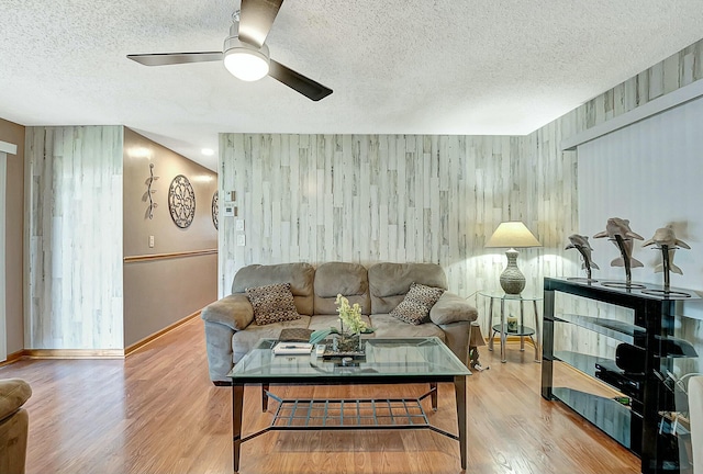 living room with ceiling fan, a textured ceiling, and light wood-type flooring