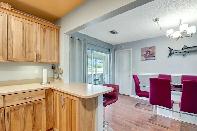 kitchen featuring light hardwood / wood-style flooring, a textured ceiling, light brown cabinetry, kitchen peninsula, and a chandelier