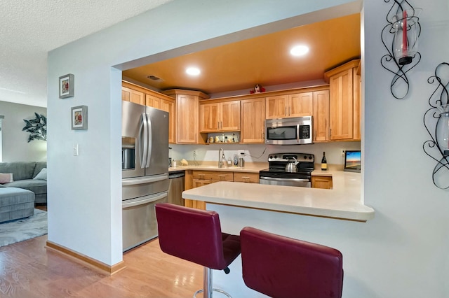 kitchen with light brown cabinetry, light wood-type flooring, kitchen peninsula, and appliances with stainless steel finishes