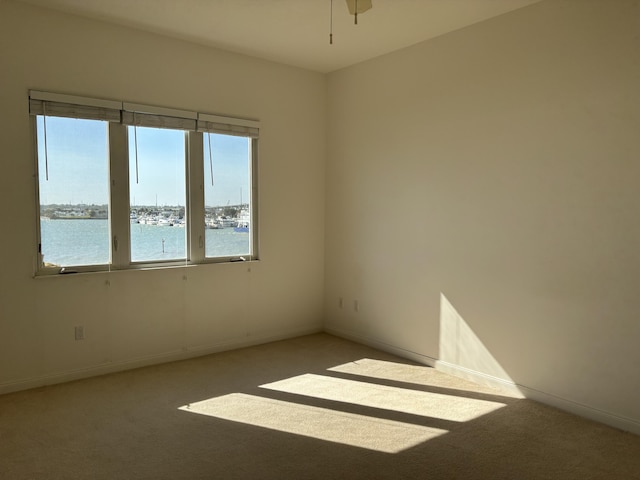 carpeted spare room with ceiling fan and a water view