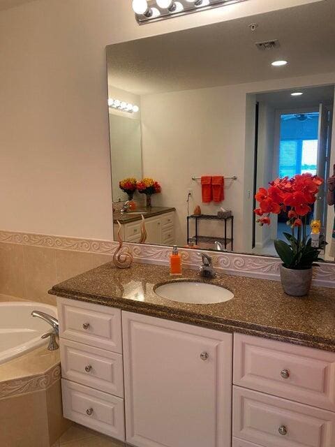 bathroom with a relaxing tiled tub, vanity, and tile patterned flooring