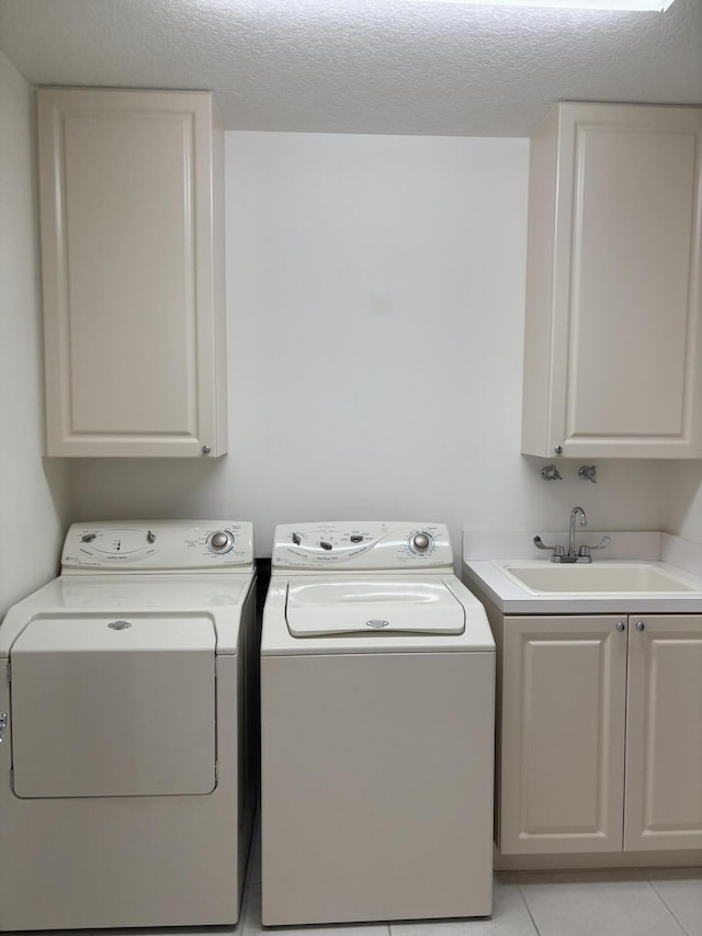 clothes washing area with washing machine and clothes dryer, sink, cabinets, a textured ceiling, and light tile patterned floors