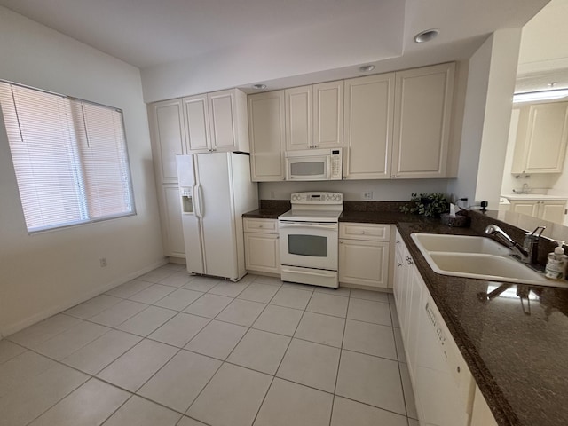 kitchen with sink, white cabinetry, light tile patterned floors, white appliances, and dark stone counters