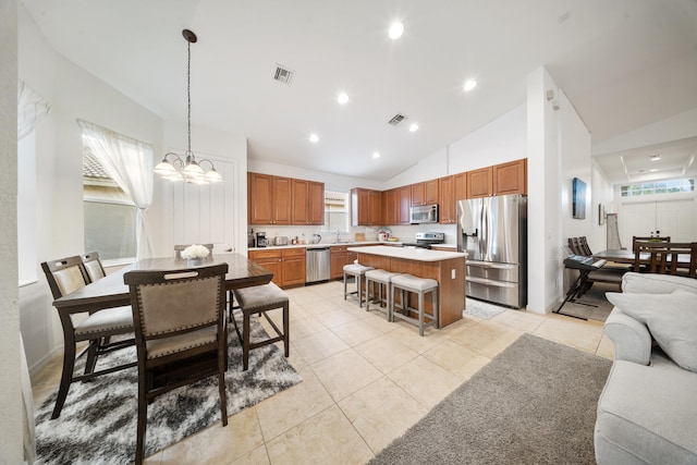 kitchen with a kitchen island, a kitchen bar, hanging light fixtures, light tile patterned floors, and stainless steel appliances