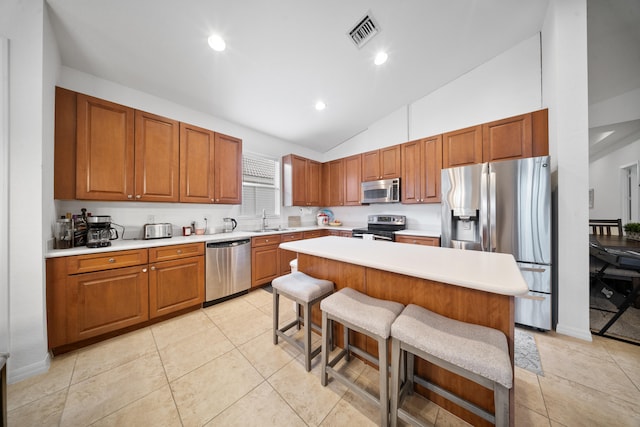 kitchen with light tile patterned flooring, a kitchen island, appliances with stainless steel finishes, sink, and a breakfast bar area