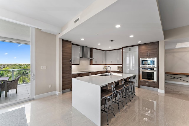 kitchen with wall chimney exhaust hood, sink, dark brown cabinets, a kitchen breakfast bar, and stainless steel appliances