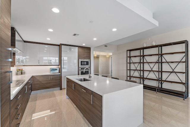 kitchen with an island with sink, built in appliances, sink, and white cabinets