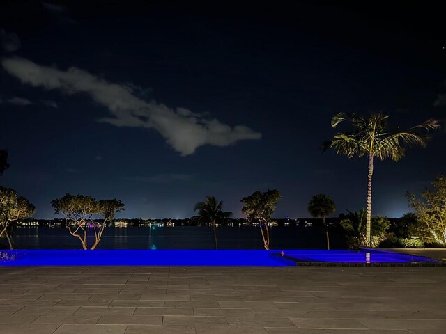 pool at night featuring a water view and a patio area