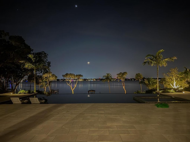 patio at night featuring a water view