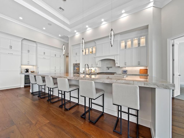 kitchen featuring a breakfast bar, white cabinetry, hanging light fixtures, a large island, and light stone counters