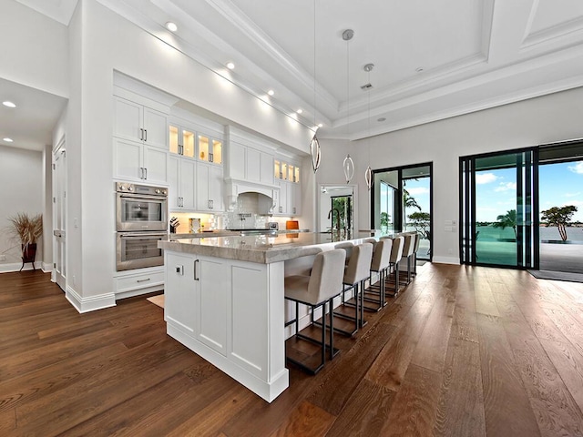 kitchen featuring a breakfast bar, pendant lighting, white cabinets, a center island, and light stone counters