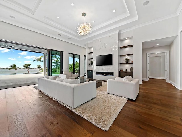 living room featuring dark wood-type flooring, an inviting chandelier, ornamental molding, built in features, and a premium fireplace