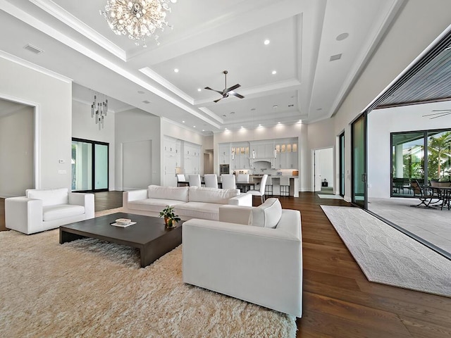 living room with dark wood-type flooring, ornamental molding, a raised ceiling, a towering ceiling, and ceiling fan with notable chandelier