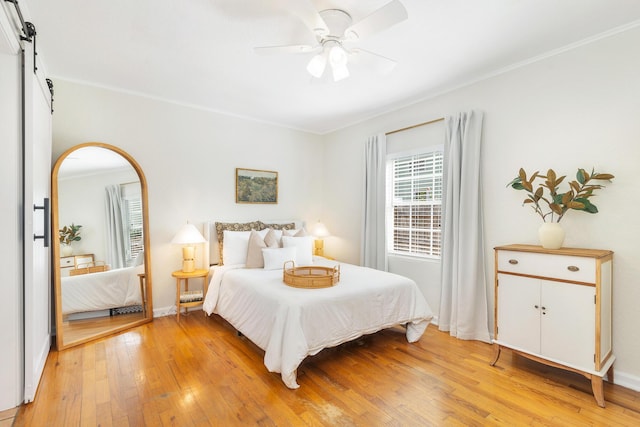 bedroom featuring crown molding, ceiling fan, a barn door, and light wood-type flooring