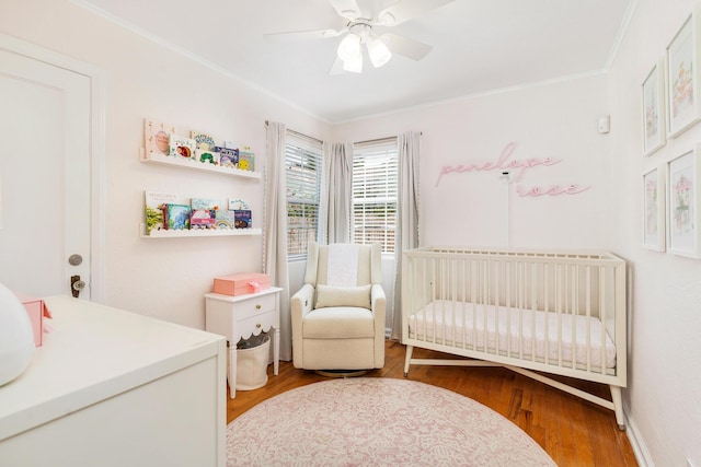 bedroom with wood-type flooring, ornamental molding, a nursery area, and ceiling fan