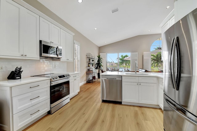 kitchen with stainless steel appliances, vaulted ceiling, sink, and white cabinets