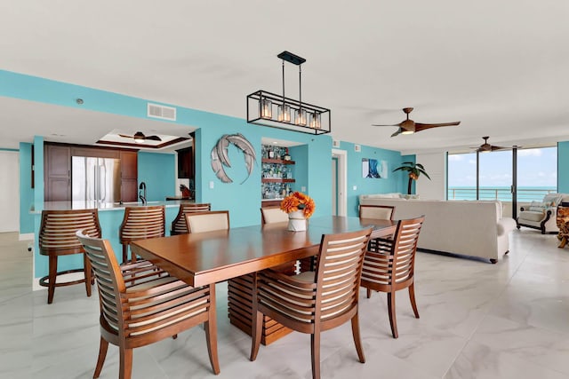 dining area with expansive windows, a water view, sink, and ceiling fan