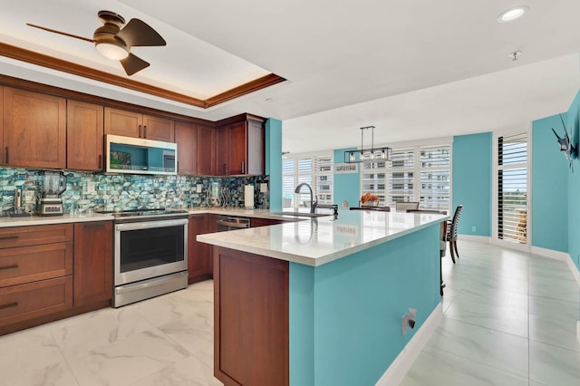 kitchen featuring appliances with stainless steel finishes, tasteful backsplash, sink, hanging light fixtures, and a tray ceiling