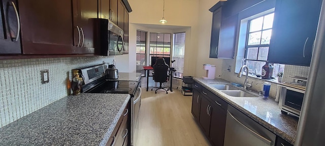 kitchen with sink, light hardwood / wood-style flooring, appliances with stainless steel finishes, pendant lighting, and dark stone counters