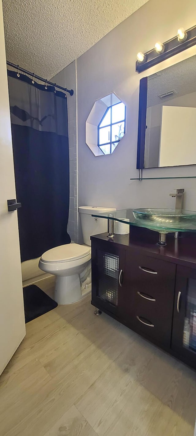 bathroom with a shower with shower curtain, vanity, wood-type flooring, a textured ceiling, and toilet