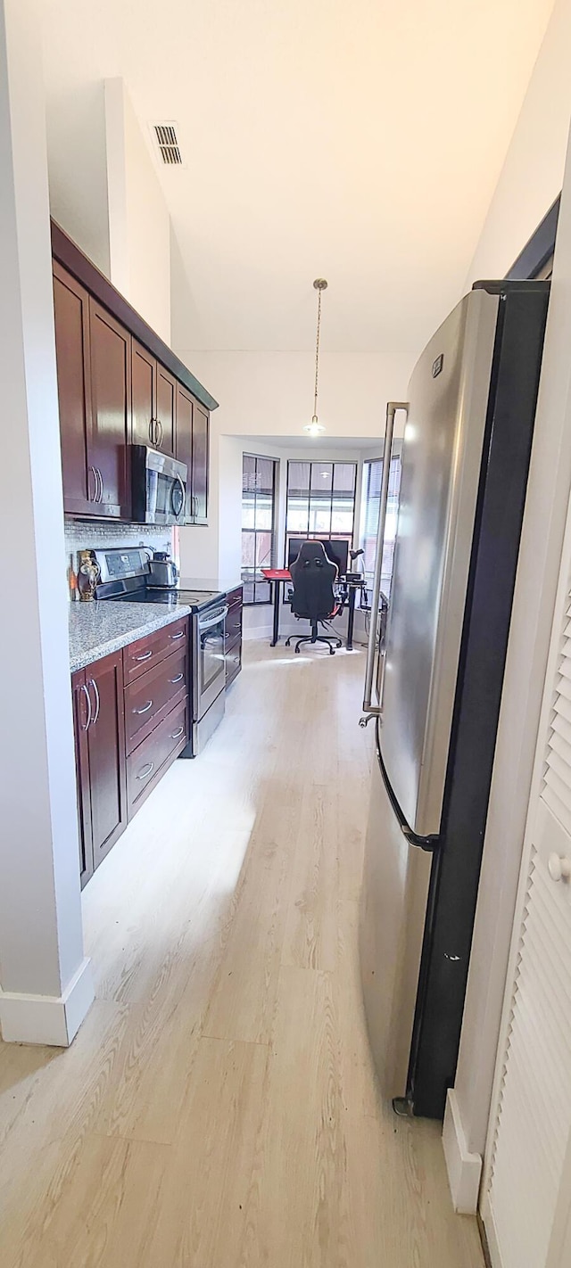 kitchen featuring vaulted ceiling, appliances with stainless steel finishes, decorative light fixtures, light stone counters, and light hardwood / wood-style floors