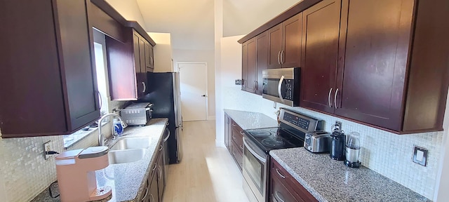 kitchen with sink, light hardwood / wood-style flooring, stainless steel appliances, light stone counters, and tasteful backsplash